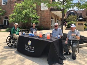 Group of seniors sitting at a Generations Senior Living table passing out cookies and lemonade