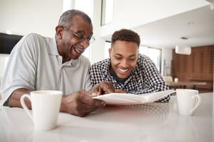 Elderly male reading a book with younger male at table