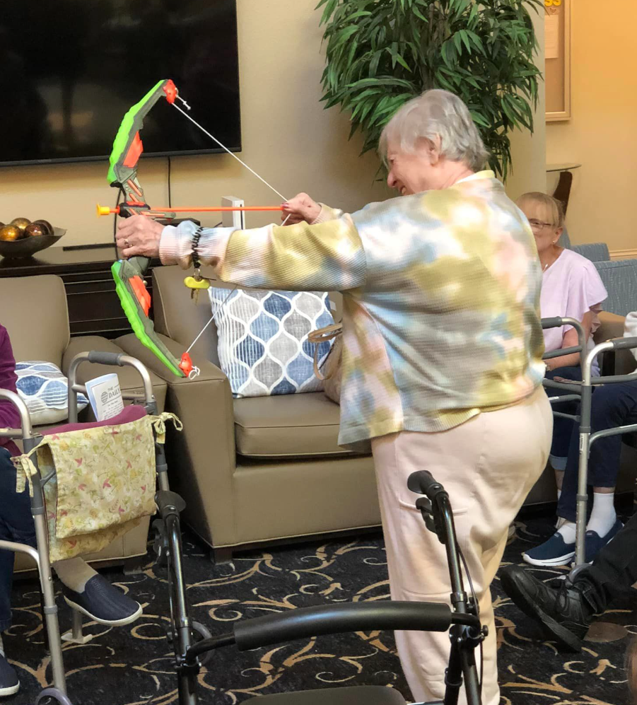 A senior woman holding a green bow and arrow, ready to launch